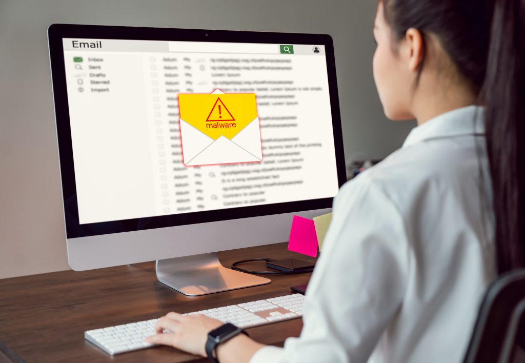 A woman sits at a computer checking her email with a malware warning on the screen.