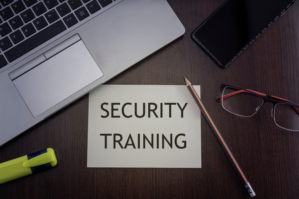 A Security Training note in the center of a desk surrounded by a laptop, pen, glasses, and phone.